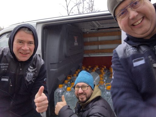 Drie mannen geven een duim omhoog voor een bus vol waterflessen.